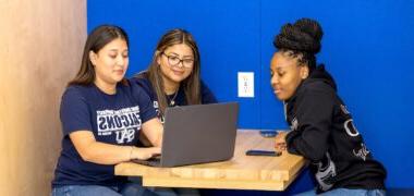 Three students in the student center looking at a laptop.